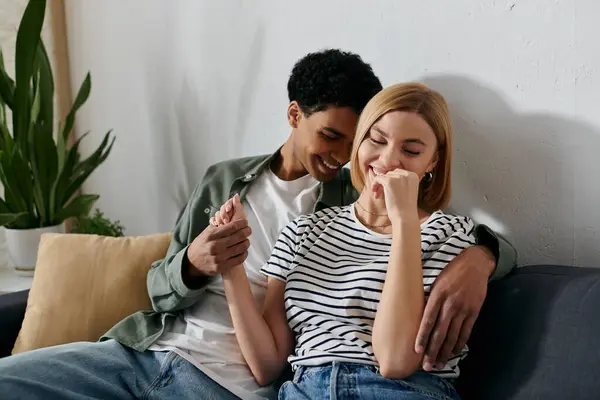 A young interracial couple sits on a couch in a modern apartment, laughing together. — Stock Photo