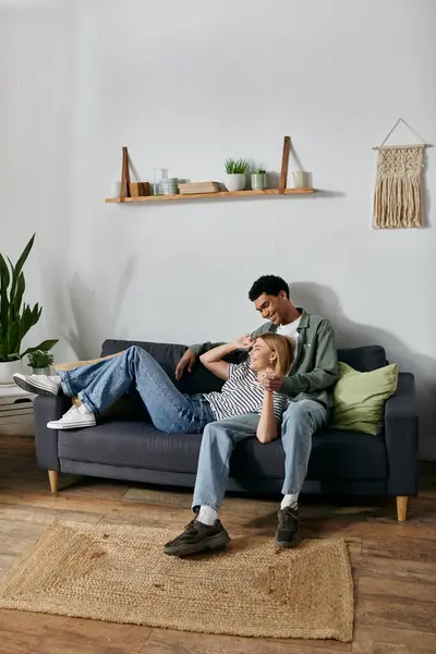 Ein junges, multikulturelles Paar entspannt sich und genießt die Gesellschaft des anderen auf einem bequemen Sofa in seiner modernen Wohnung. — Stockfoto