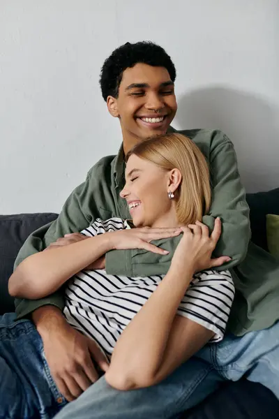 Un jeune couple, un homme et une femme, rient et s'embrassent sur un canapé dans un appartement moderne. — Photo de stock