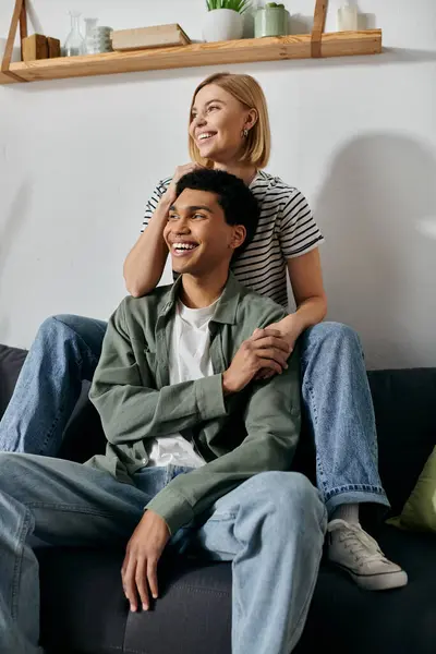 A young multicultural couple sits on a couch in a modern apartment, smiling and enjoying each others company. — Stock Photo