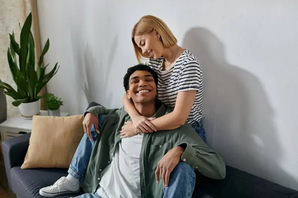 A young interracial couple relaxes on a couch in a modern apartment, enjoying a moment of intimacy and affection. — Stock Photo