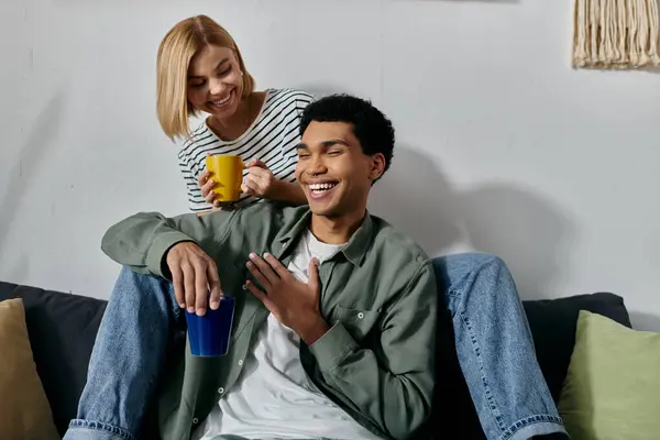 A young interracial couple relaxes on a couch in a modern apartment, enjoying a cup of coffee and each others company. — Stock Photo