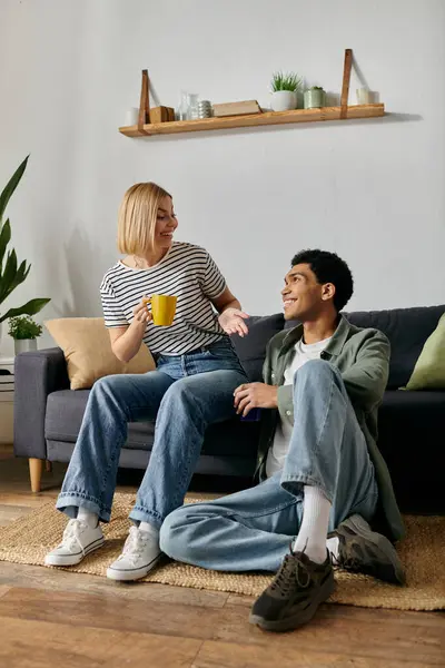 A young, multicultural couple relaxes in their apartment, sharing a cozy moment and a warm drink. — Stock Photo