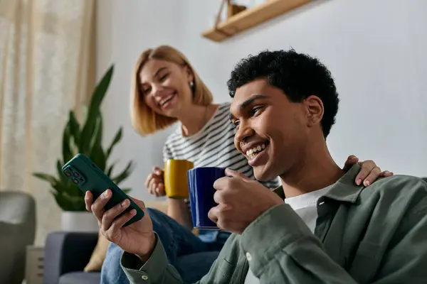 A young multicultural couple enjoys a relaxing moment in their modern apartment, laughing and sharing a cup of coffee. — Stock Photo