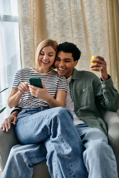 A young interracial couple share a laugh while looking at their phone in their modern apartment. — Stock Photo