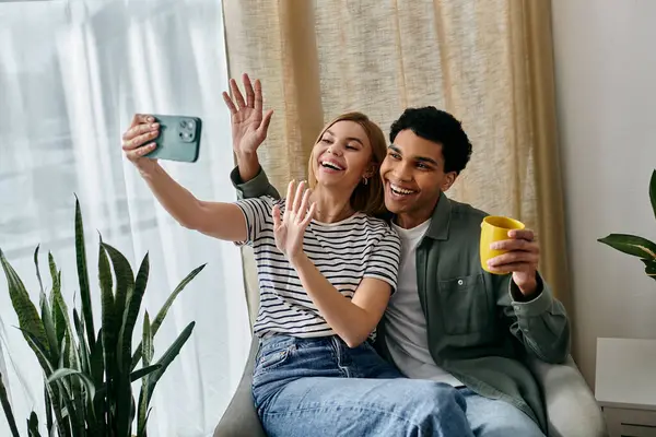 A young, multicultural couple smiles for a selfie in their modern apartment, showcasing a relaxed and intimate moment. — Stock Photo