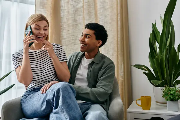 A young couple, laughing and enjoying each others company, sits in a modern apartment with a plant in the background. — Stock Photo