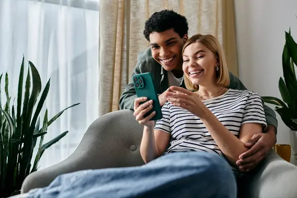 A young couple shares a laugh while looking at a smartphone in their modern living room. — Stock Photo