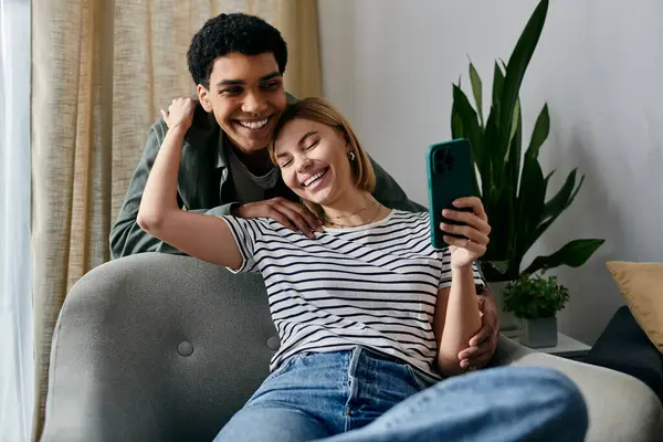 A young interracial couple laughs together in a modern apartment while holding a smartphone. — Stock Photo