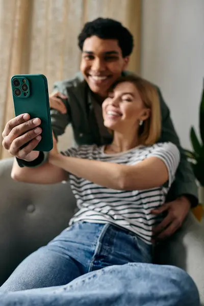 A young interracial couple smiles and takes a selfie together in their modern apartment. — Stock Photo