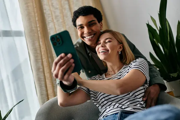 A young multiracial couple happily takes a selfie in a modern apartment, smiling and enjoying each others company. — Stock Photo