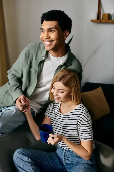 Um jovem casal interracial sorri um para o outro, desfrutando de uma tarde relaxada em seu apartamento moderno. — Fotografia de Stock