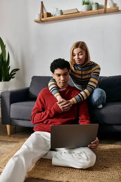 A happy interracial couple relaxes on the floor of their apartment while using a laptop. — Stock Photo