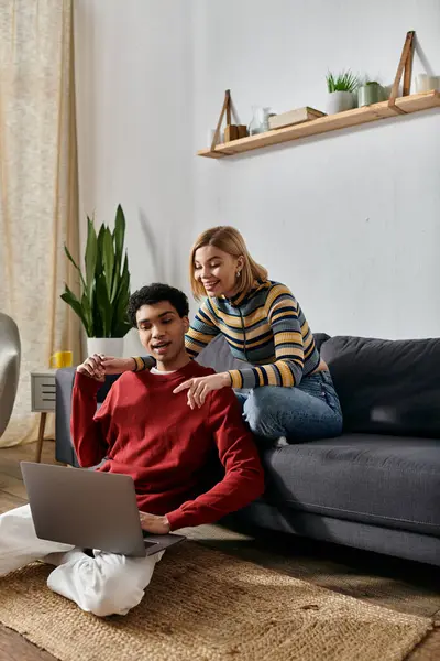 A diverse couple spending time in a modern apartment; the woman on the sofa and the man on the floor working on a laptop. — Stock Photo