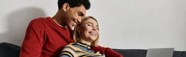 A happy multicultural couple shares a laugh together on a comfortable sofa in their modern apartment. — Stock Photo