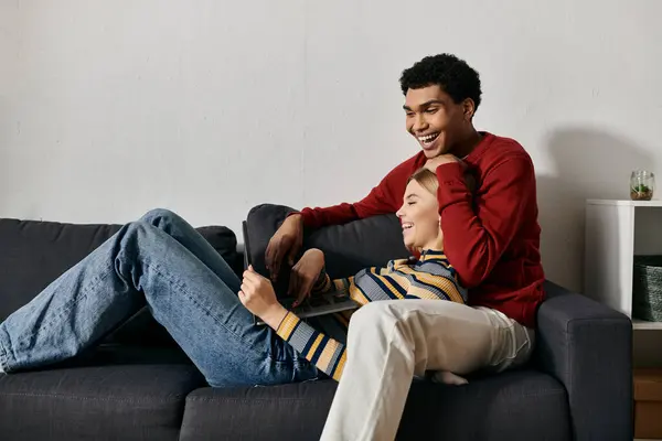 A diverse couple joyfully bonds in their sleek apartment, laughing and using a laptop together. — Stock Photo