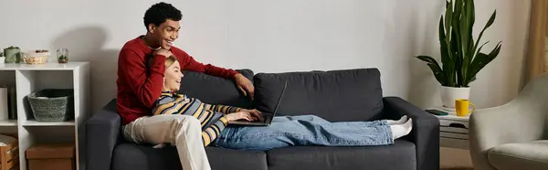 A happy, multicultural couple enjoys a relaxing evening together on a couch in their modern apartment. — Stock Photo