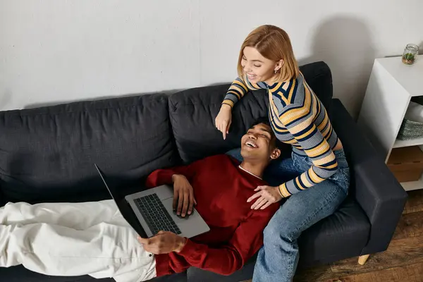 A happy multicultural couple enjoys a cozy evening together on their couch, sharing laughter and using a laptop. — Stock Photo