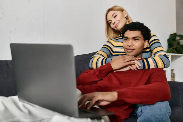 Um casal multicultural feliz relaxa em um sofá em um apartamento moderno, desfrutando de tempo de qualidade juntos enquanto navega em um laptop. — Fotografia de Stock