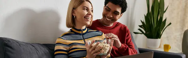 A multicultural couple laughs together while enjoying a movie night at home. — Stock Photo