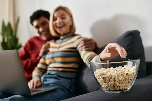 A happy, multicultural couple relaxes on a couch in a modern apartment, enjoying a movie night together. — Stock Photo