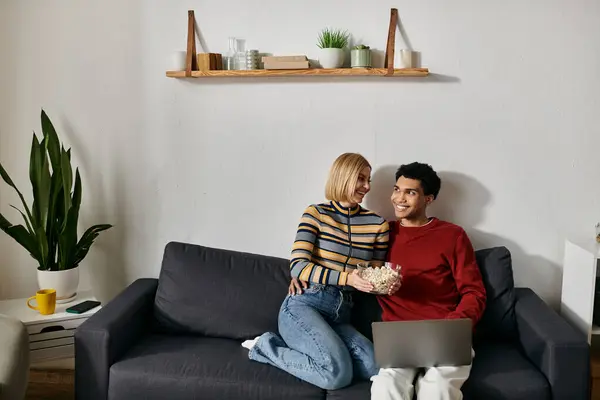 A happy multicultural couple enjoys a relaxing evening together in their modern apartment, sharing popcorn and a laptop. — Stock Photo