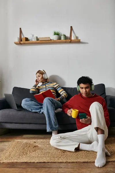 A happy multicultural couple relaxes in a modern apartment, enjoying coffee and using their phones. — Stock Photo