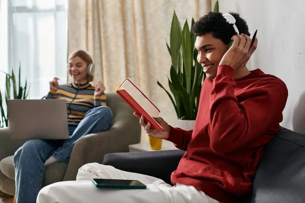 A happy multicultural couple relaxes at home, one reading a book and the other enjoying music. — Stock Photo