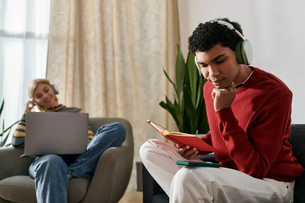Multicultural couple relax at home in modern apartment. Man reads with headphones, woman works on laptop. — Stock Photo