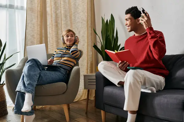 Una felice coppia multiculturale si gode un pomeriggio di relax nel loro appartamento, uno lavorando sul loro computer portatile, l'altro leggendo un libro. — Foto stock