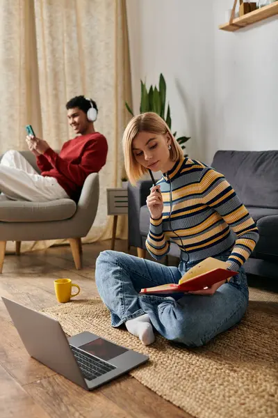 Un jeune couple se détend dans leur appartement moderne : elle lit assise sur le sol, tandis qu'il se prélasse dans un fauteuil avec un casque. — Photo de stock