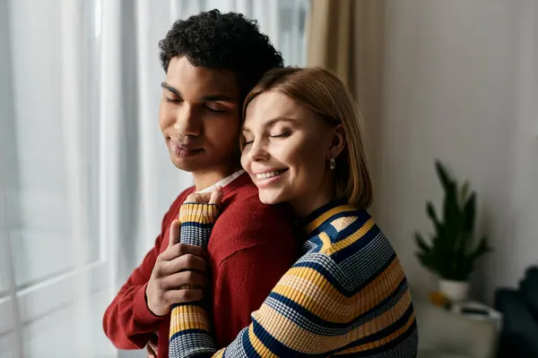 Una feliz pareja multicultural se abraza en un apartamento moderno, lleno de calidez y amor. - foto de stock
