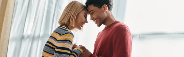 Una pareja multicultural sonríe brillantemente en su apartamento moderno. - foto de stock