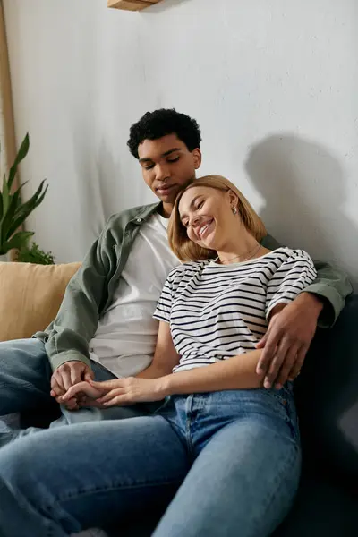 A young interracial couple relaxes on a couch in a modern apartment, enjoying each others company. — Stock Photo