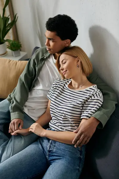 A young interracial couple relaxes on a couch in their modern apartment, enjoying a quiet moment together. — Stock Photo