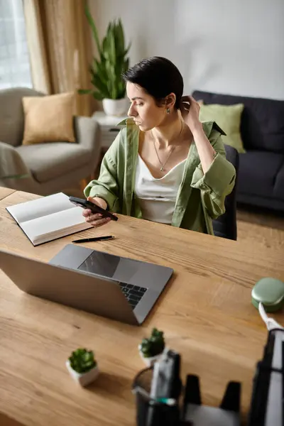 A woman works remotely at her home desk, using her laptop and phone. — Stock Photo
