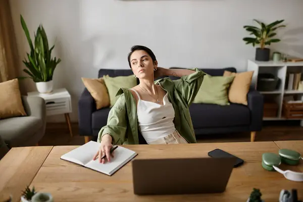 Eine Frau sitzt an ihrem Schreibtisch im Home Office, arbeitet an einem Laptop und macht sich Notizen in einem Notizbuch. — Stockfoto