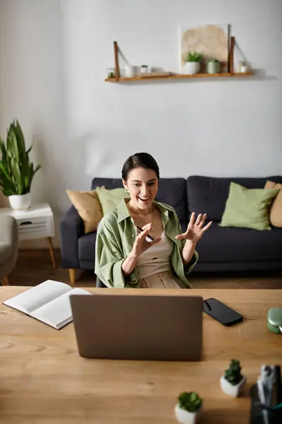 A woman sits at her home office desk, smiling and gesturing while on a video call. — Stock Photo