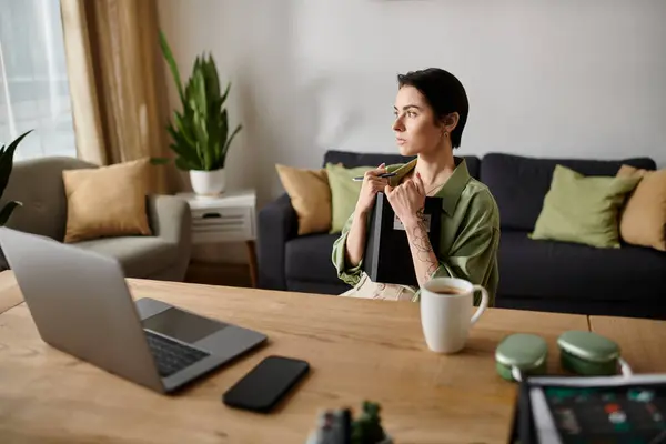 A woman is working from home, sitting at a desk with a laptop, coffee, and a notebook. — Stock Photo