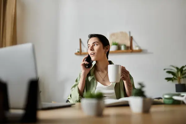 A woman sits at her desk, talking on the phone while holding a mug of coffee. — Stock Photo