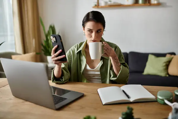 A woman works from home, taking a break to sip coffee and look at her phone. — Stock Photo