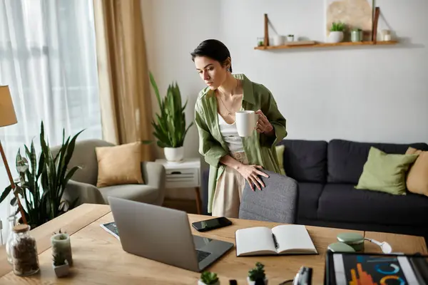 A young woman stands at her home office desk, taking a moment to relax with a cup of coffee. — Stock Photo