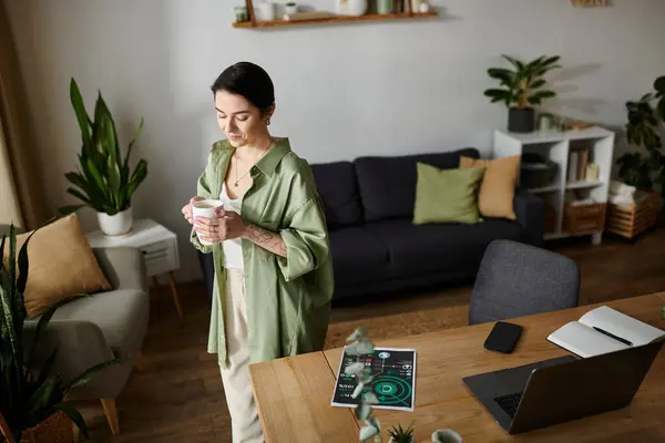 Una donna sta accanto alla scrivania, prendendo una pausa dal lavoro con una tazza di caffè in mano. — Foto stock