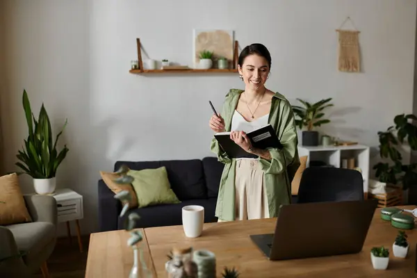 A woman smiles as she holds a notebook and pen while standing in her living room. — Stock Photo