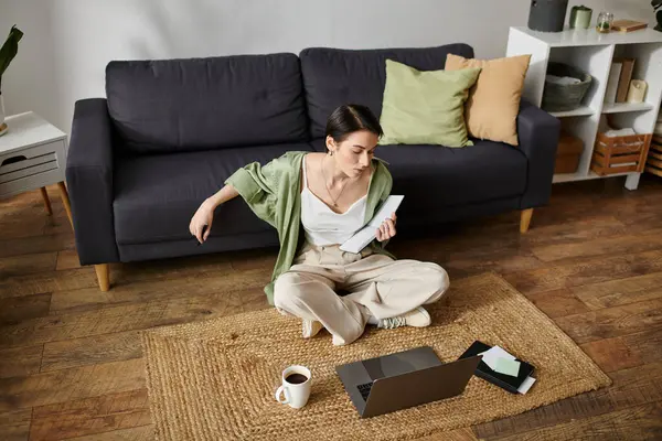 A woman sits on a rug in her home, working on a laptop. — Stock Photo