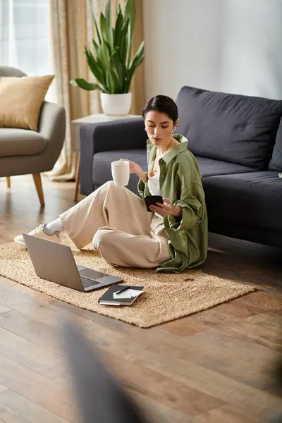 A woman sits on the floor with a laptop, a cup of coffee, and a phone. — Stock Photo