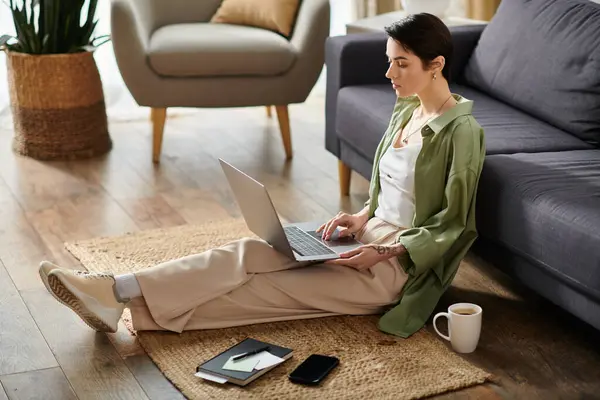 An attractive woman sits on a rug in her home, working on her laptop. — Stock Photo