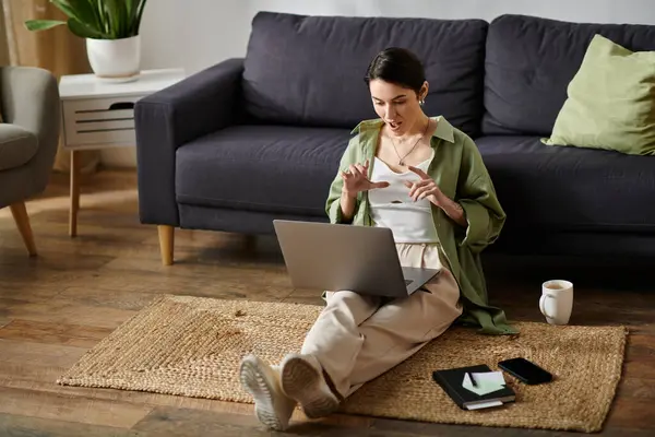 A woman sits on a rug in her home, working on her laptop. — Stock Photo