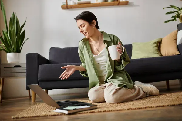 A woman working remotely from home, sitting on the floor with her laptop and a mug of coffee. — Stock Photo