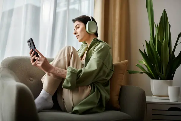 A woman relaxes on a couch with headphones and a phone, working remotely. — Stock Photo